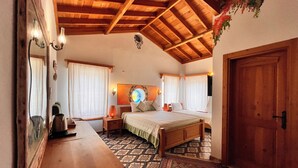 Een slaapkamer met een houten plafond, een bed, een nachtkastje, een tafel en een kamerbreed tapijt met een patroon.