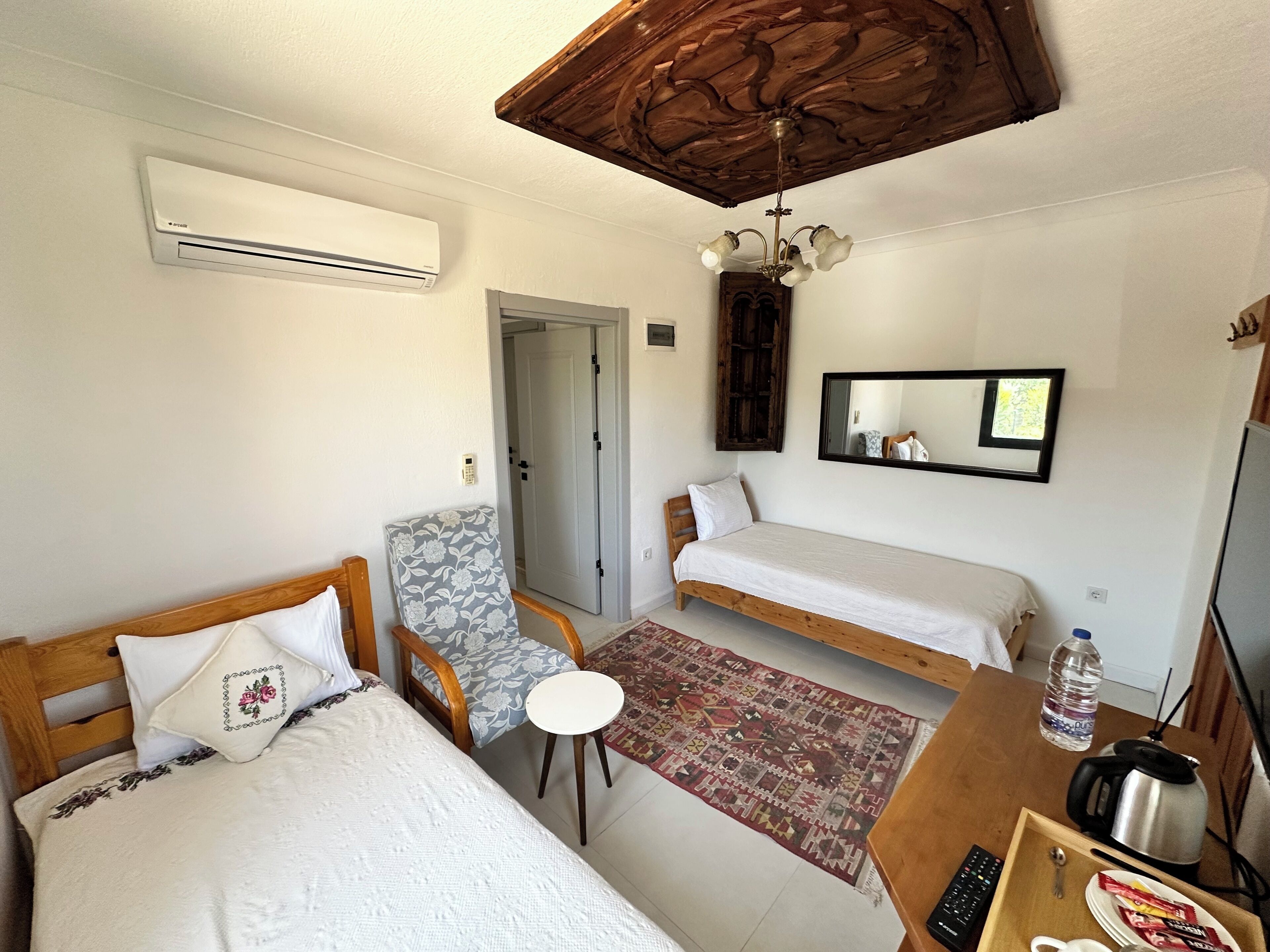 A bedroom with two beds, a chair, a small table, a kettle, a water bottle, and a mirror.