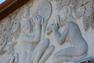 Un detallado grabado en piedra de una figura reclinada, un espejo y racimos de uvas.