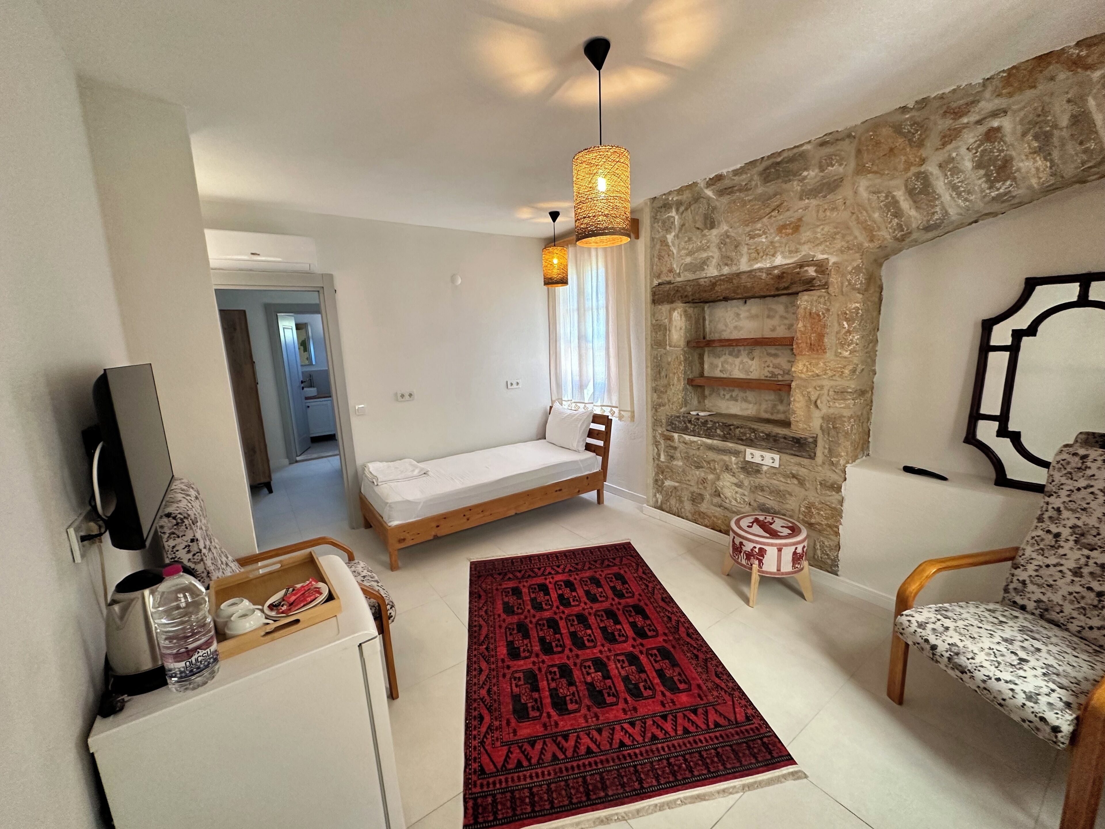 A compact living space with a bed, a sofa, a small rug, a stone wall, and a television.