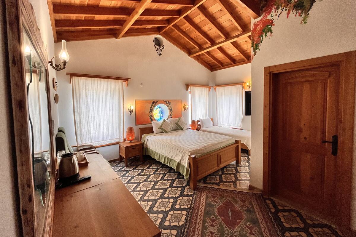 A cozy bedroom with a wooden ceiling, a bed, a nightstand, a table, and a patterned rug.