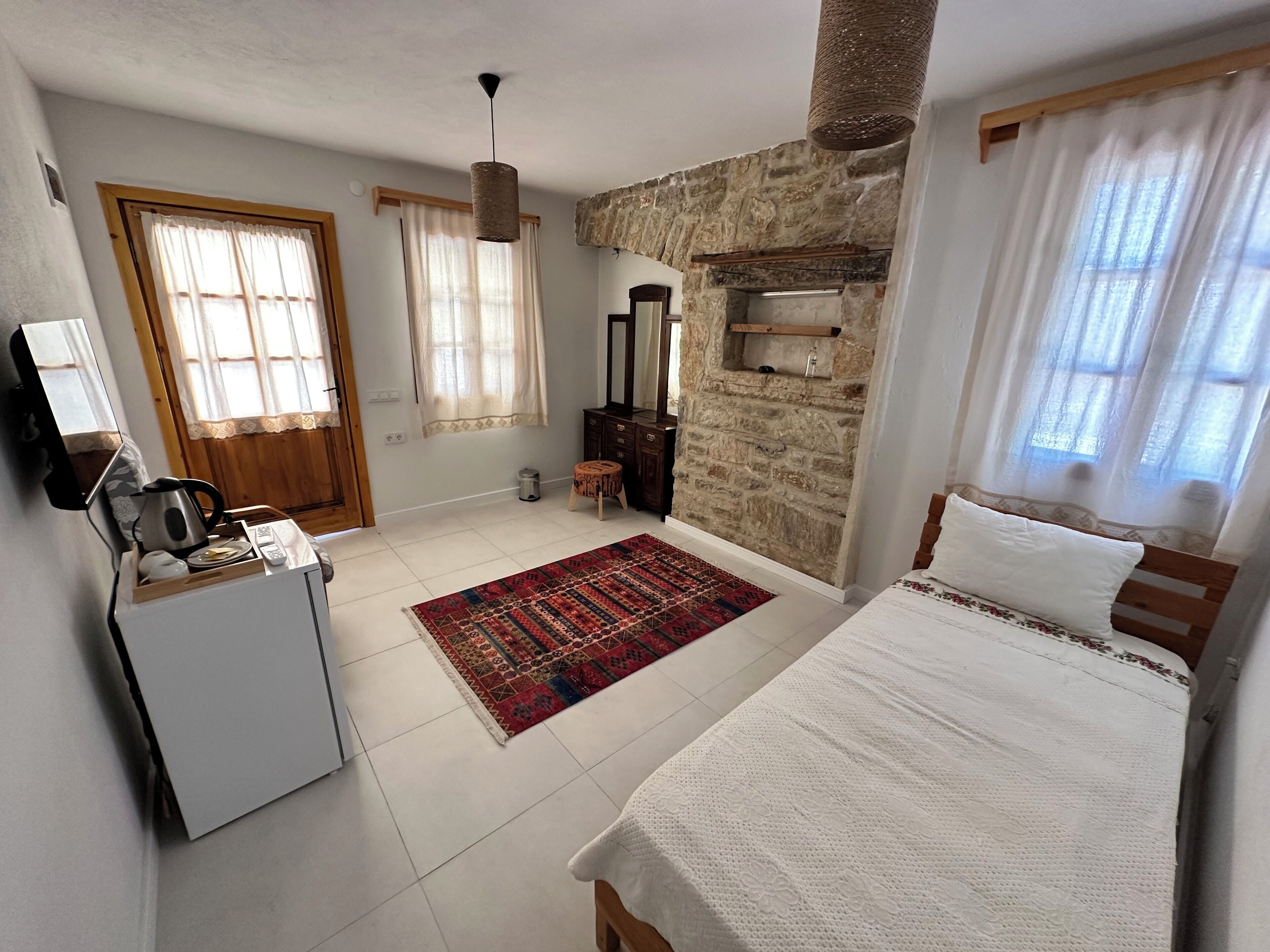 Quarto com cama, penteadeira, espelho, pequena mesa com chaleira e tapete.