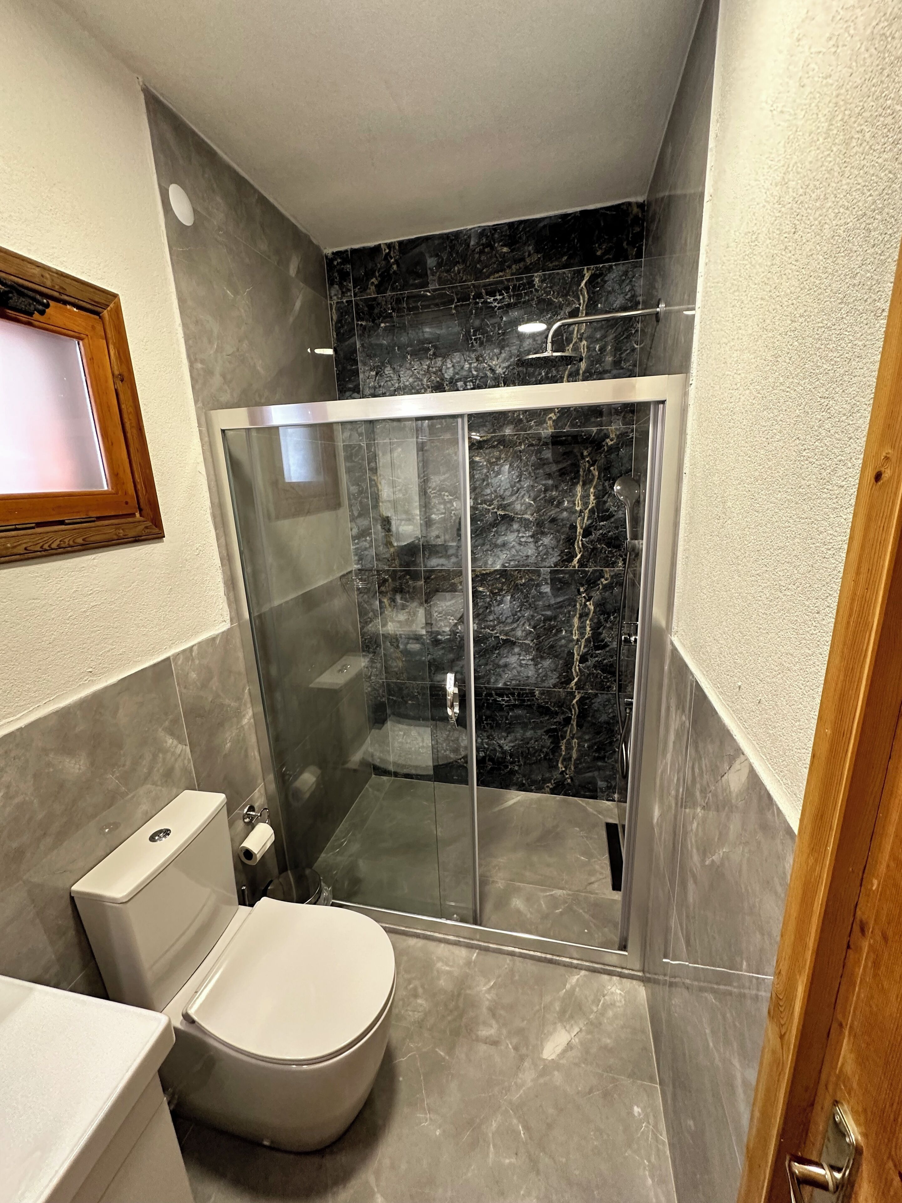 A modern bathroom with a glass-enclosed shower, a toilet, and a sink.