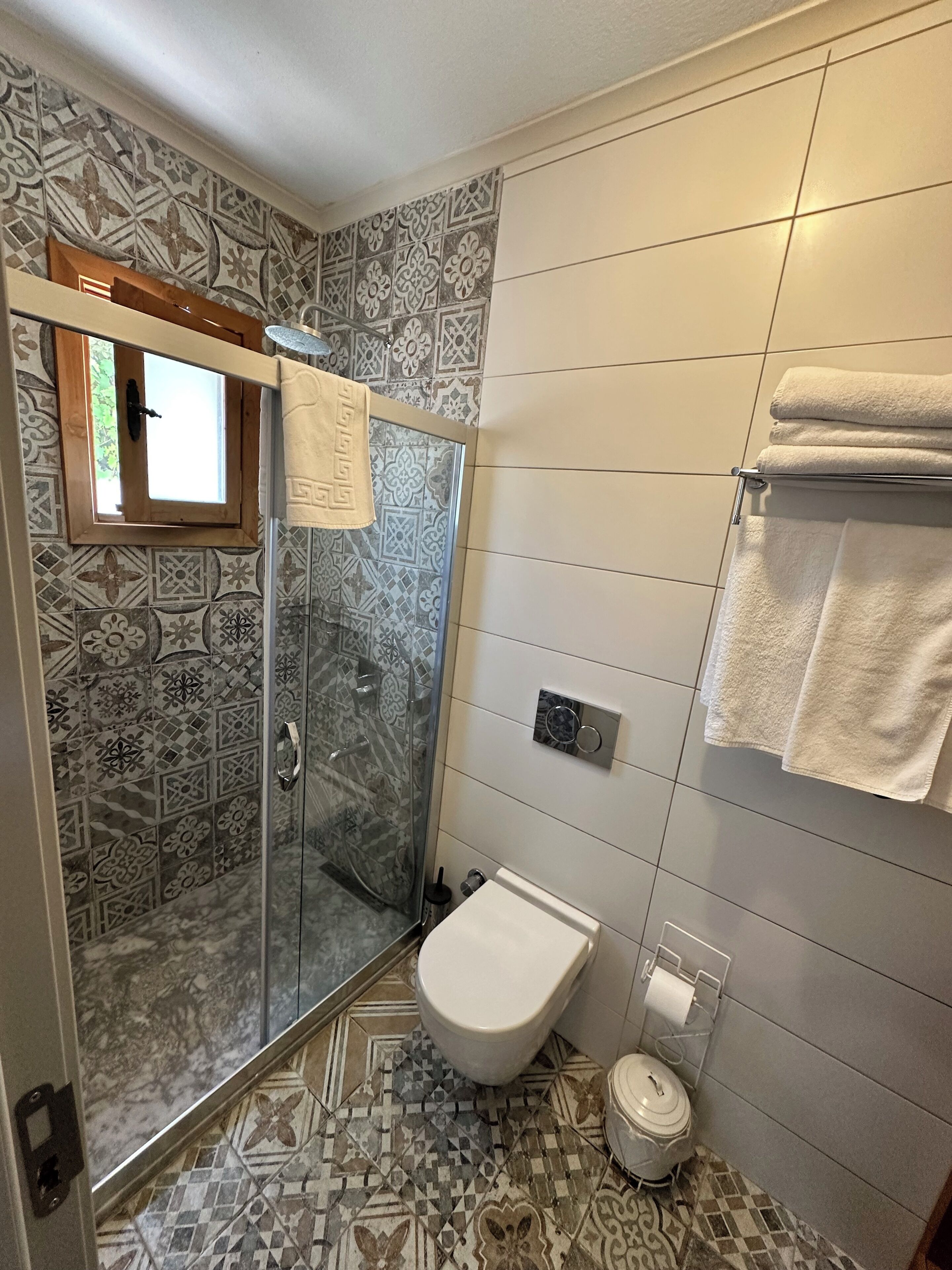 A bathroom with patterned tiles, a glass shower enclosure, a toilet, and a towel rack.