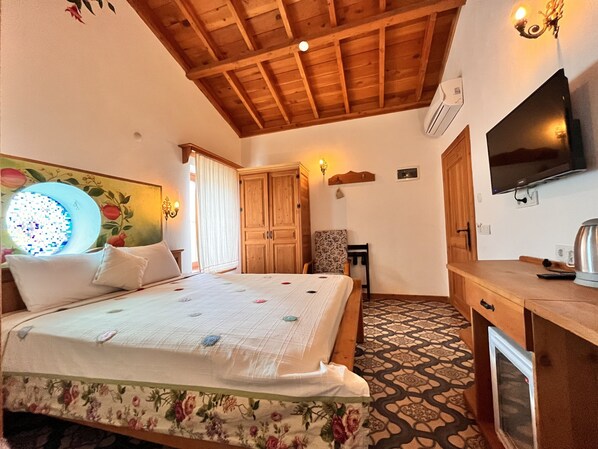 A bedroom with a wooden ceiling, a bed with floral bedding, a chair, a desk, and a television.