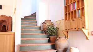 Een trap met terracottategels, een grote terracotta pot en een houten boekenkast vol boeken.