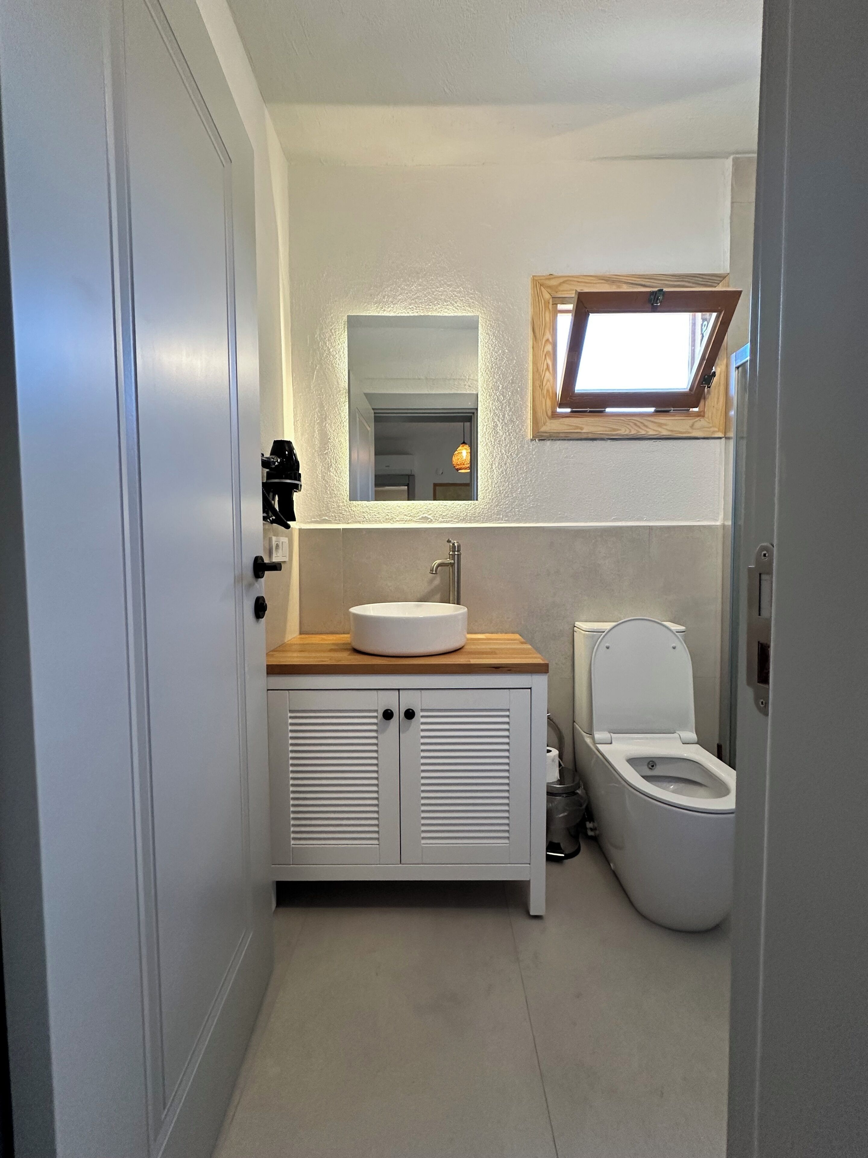 Ein Badezimmer mit einem weißen Waschbecken, einer Holztischplatte und einer Toilette.