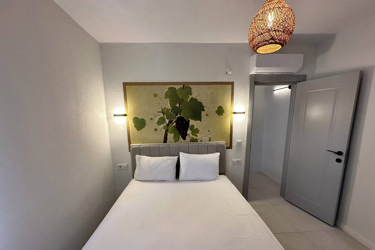 A hotel room with a bed, a wall-mounted light fixture, and a door.