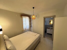 Un dormitorio con cama, lámpara de noche, ventana con cortinas y vistas al baño.