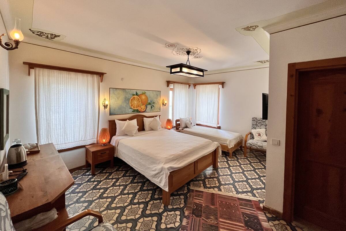 A hotel room with a large bed, two bedside tables, a desk, and a chair. There is a painting on the wall and a patterned carpet.