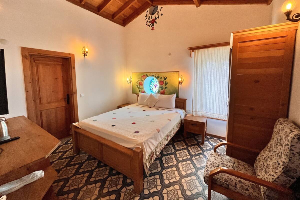 A bedroom with a wooden bed, a bedside table, a chair, and a wooden wardrobe.