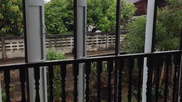 Un'area esterna riparata con ringhiera in legno, una sedia in vimini e vista su un giardino e edifici sullo sfondo.