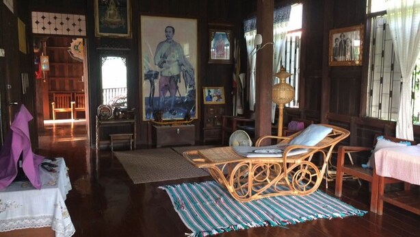 Quarto de madeira tradicional com sofá de vime, uma mesa pequena e um banco. Há quadros nas paredes e um quadro grande.