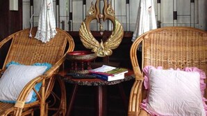 Duas cadeiras de vime com almofadas, uma mesinha com livros, e um objeto dourado decorativo entre elas.