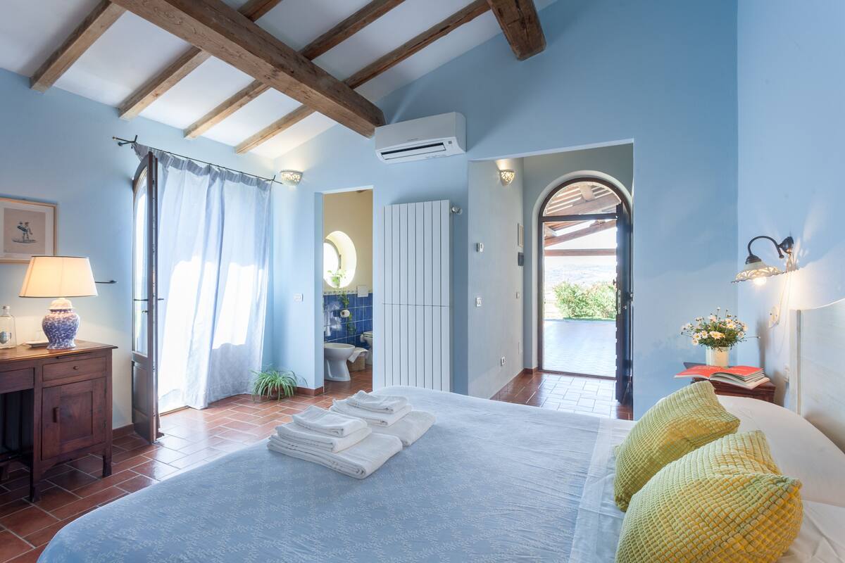 Een slaapkamer met een bed, handdoeken, een bureau, een lamp en uitzicht op de badkamer.