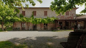 Un bâtiment en pierre avec une cour en gravier, des volets en bois et des plantes en pot.
