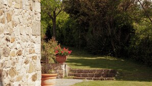 Un bâtiment en pierre avec un chemin pavé menant à une zone herbeuse où se trouve un grand bac rempli de fleurs rouges.