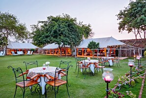 An outdoor dining area with tables and chairs, surrounded by trees and a stone wall. - Ramathra Fort (Sapotra)