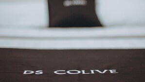 Vista borrosa de una cama con una etiqueta y el texto "DS COLIVE" en la colcha.