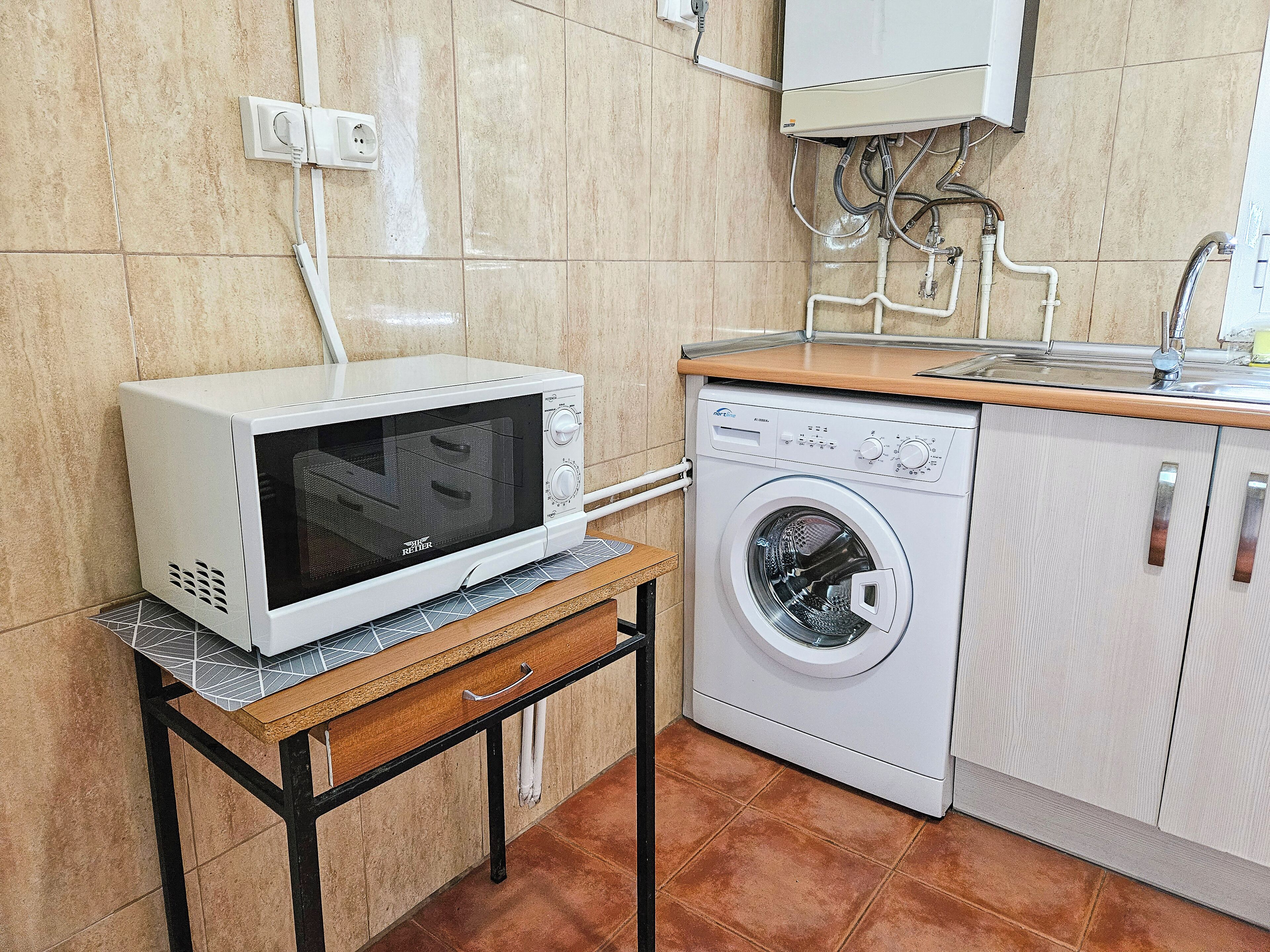 A compact kitchen with a microwave and a washing machine on a wooden countertop.