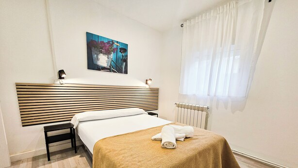 A hotel room with a bed, a bedside table, a headboard, a window with curtains, a radiator, and a wall-mounted artwork. - Complejo Bubal Formigal 3000 (Biescas)