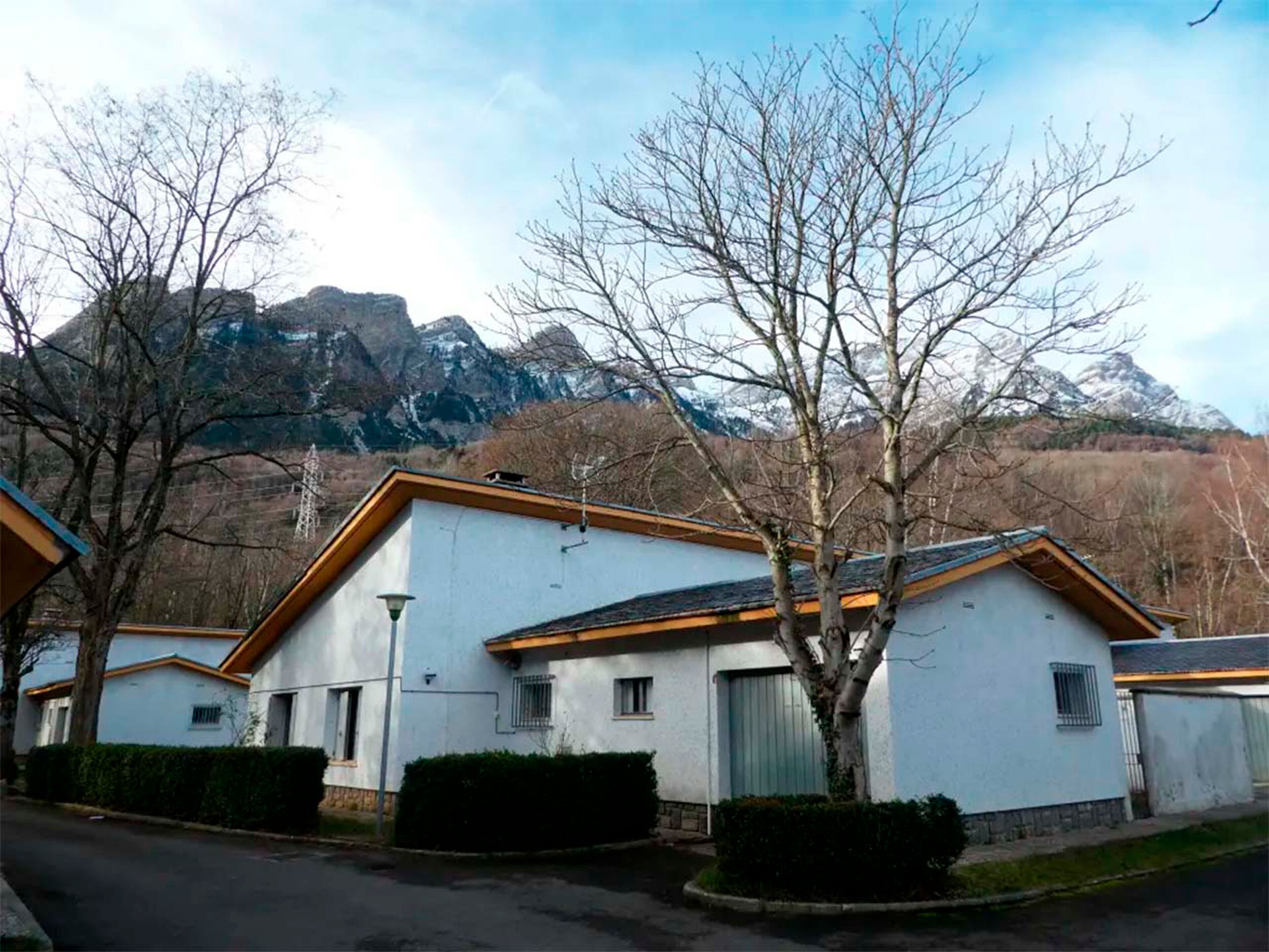 Una hilera de edificios blancos con techos marrones, rodeados de árboles desnudos y una montaña al fondo.