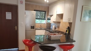 Eine kleine Küche mit Kühlschrank, Spüle und einer Essecke mit Hockern.
