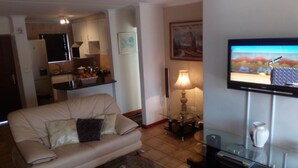 Ein Wohnzimmer mit einer Couch, einem Fernseher, einer Lampe und einer Küche im Hintergrund.