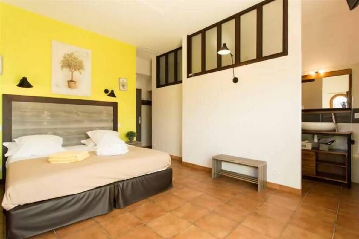 A bedroom with a bed, a bench, a bedside table, a mirror, and a potted plant.