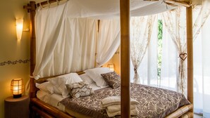 A four-poster bed with white and patterned bedding, a bedside lamp, and a view of greenery through sheer curtains. - Mas Picton (Argelès-sur-Mer)