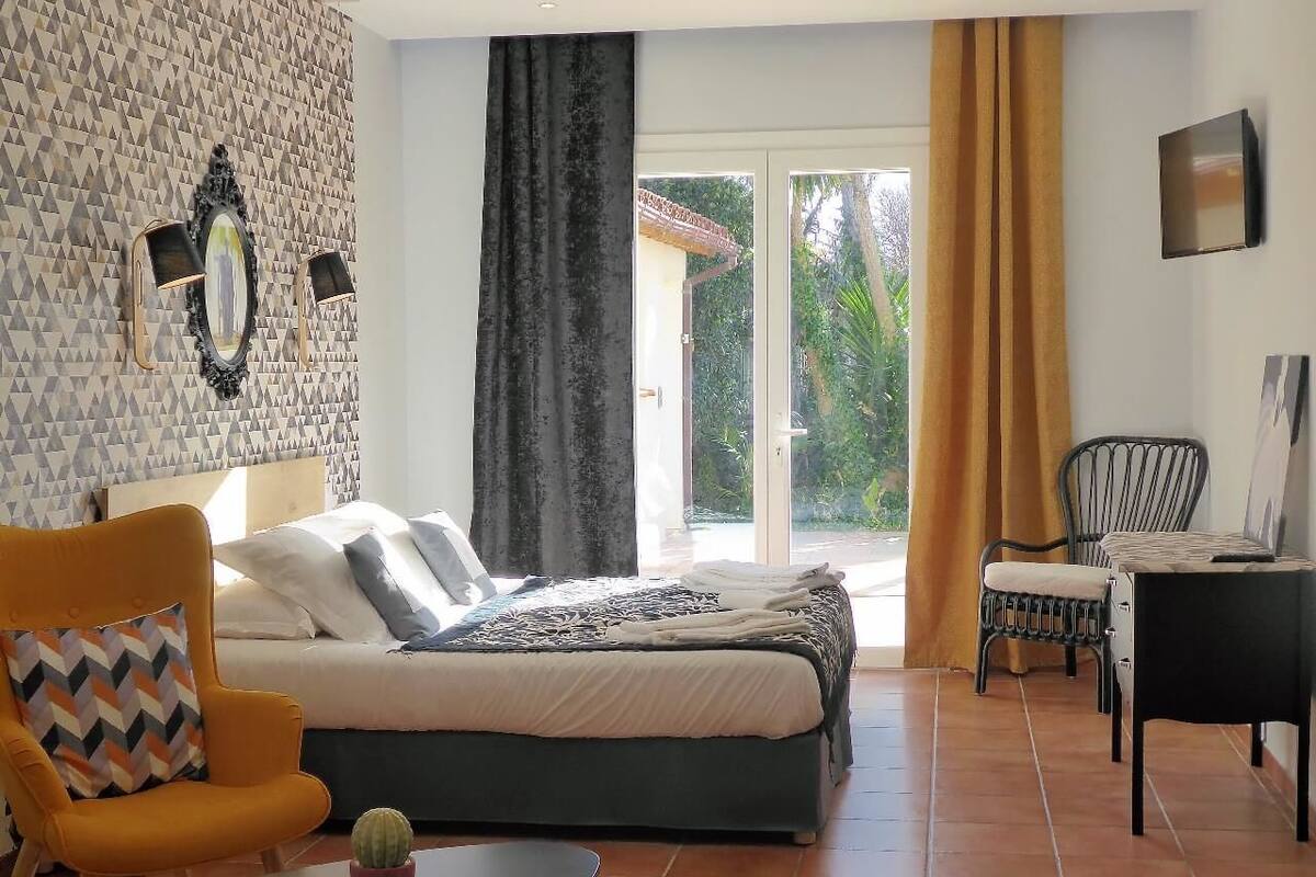 A bedroom with a bed, a sofa, a chair, a small table, and a window with curtains.