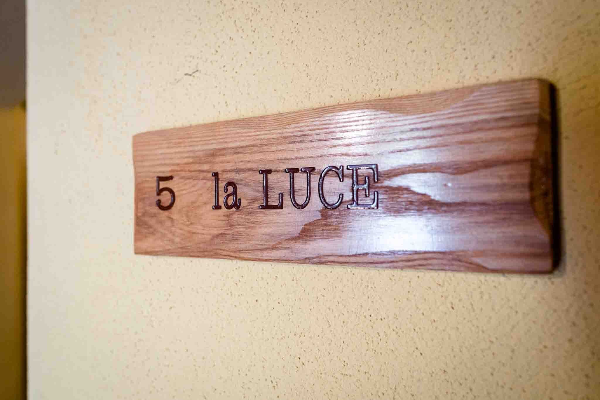 Une enseigne en bois portant l’inscription « 5 LA LUCE » est fixée à un mur.