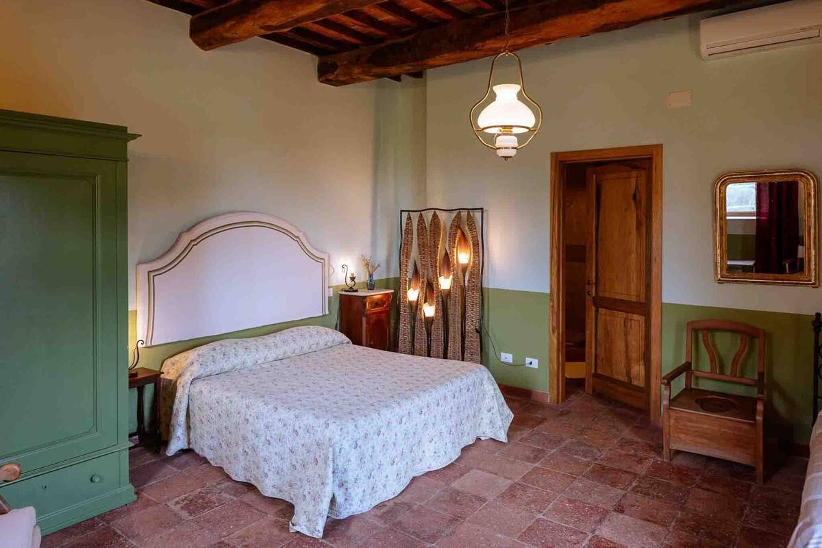 Un dormitorio con cama, una silla de madera, un espejo y una lámpara colgante.