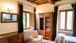 Una habitación acogedora con un aparador de madera, una silla, una cama con colcha a rayas y un espejo grande en la pared.
