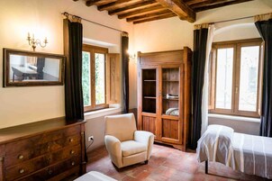 A cozy room with a wooden cabinet, a chair, a bed with a striped bedspread, and a large mirror on the wall.