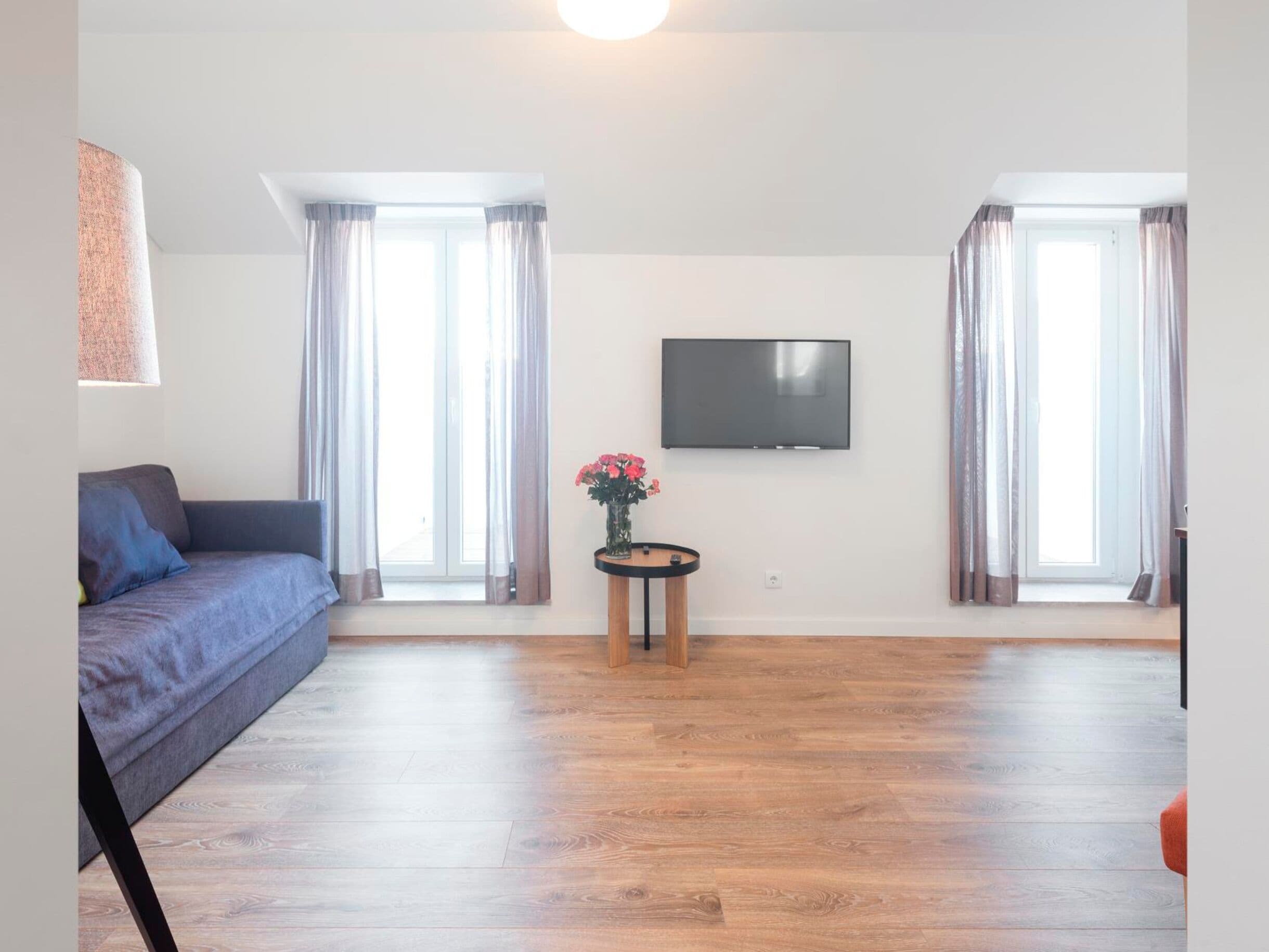 Una sala de estar con un sofá, un televisor montado en la pared y una mesita con un florero.