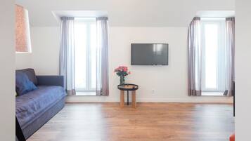 A living room with a sofa, a TV mounted on the wall, and a small table with a vase of flowers.