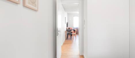 A narrow hallway with a wooden floor, white walls, and a bed on the right.