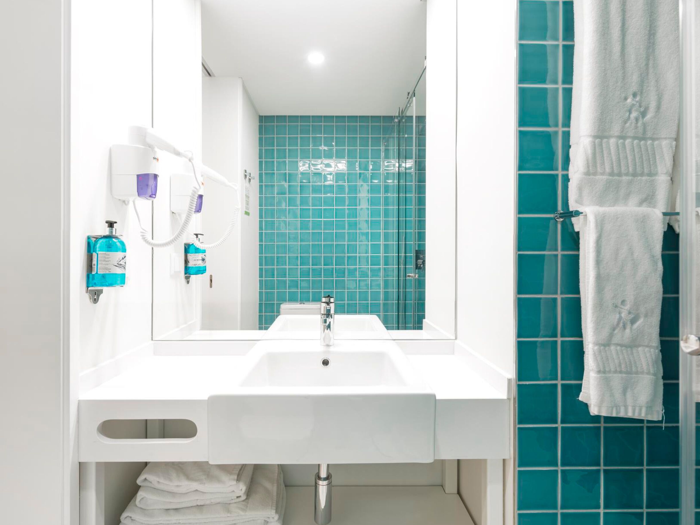 A modern bathroom with a white sink, a mirror, and a blue tiled wall.