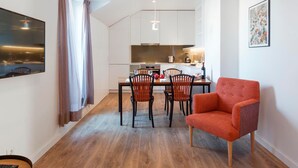 A modern apartment with a dining area, kitchen, and a red armchair.