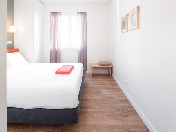 Habitación de hotel con cama, una mesita, ventana con cortinas y cuadros en la pared.