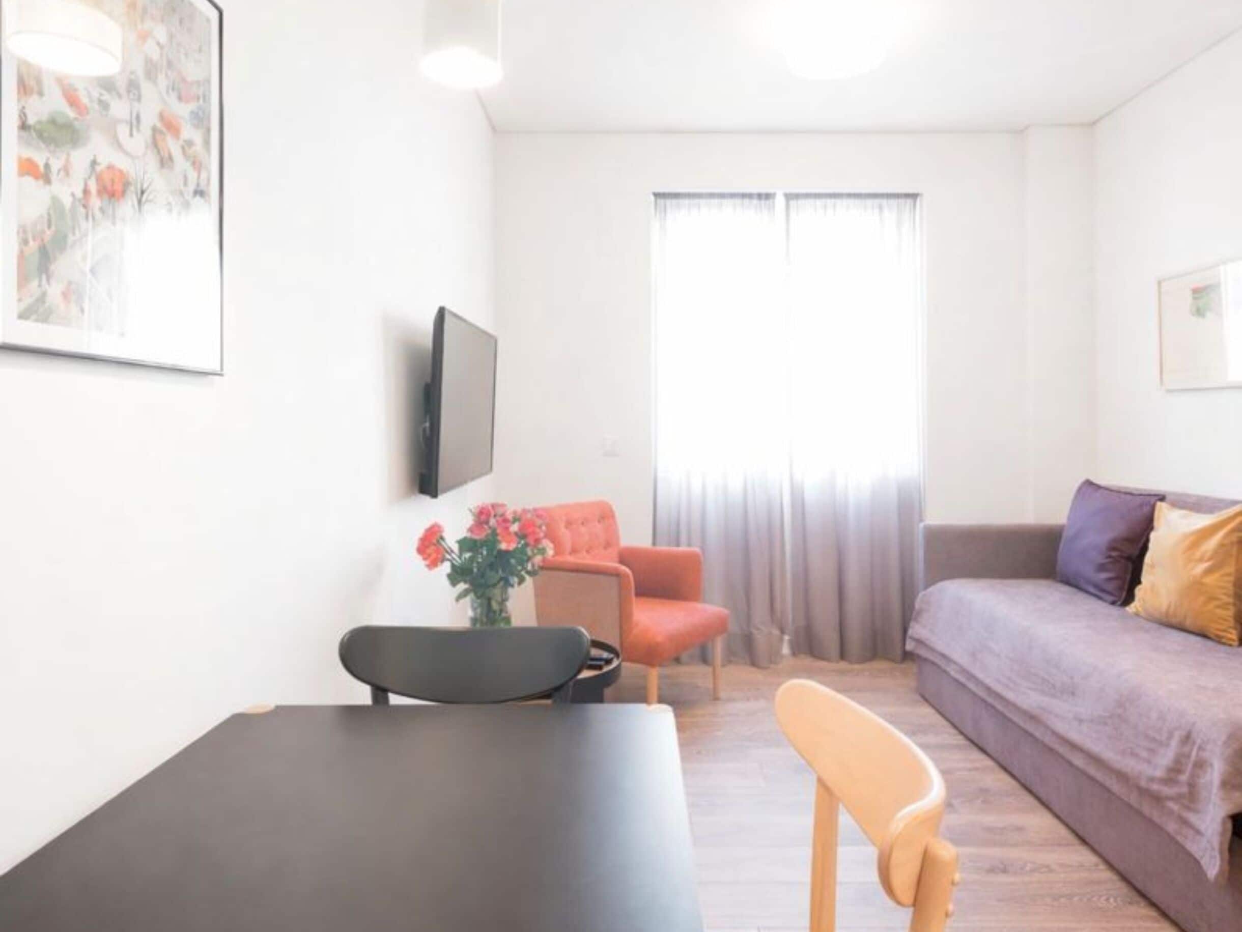 Una sala de estar moderna con un sofá, una mesa de comedor y un televisor montado en la pared.