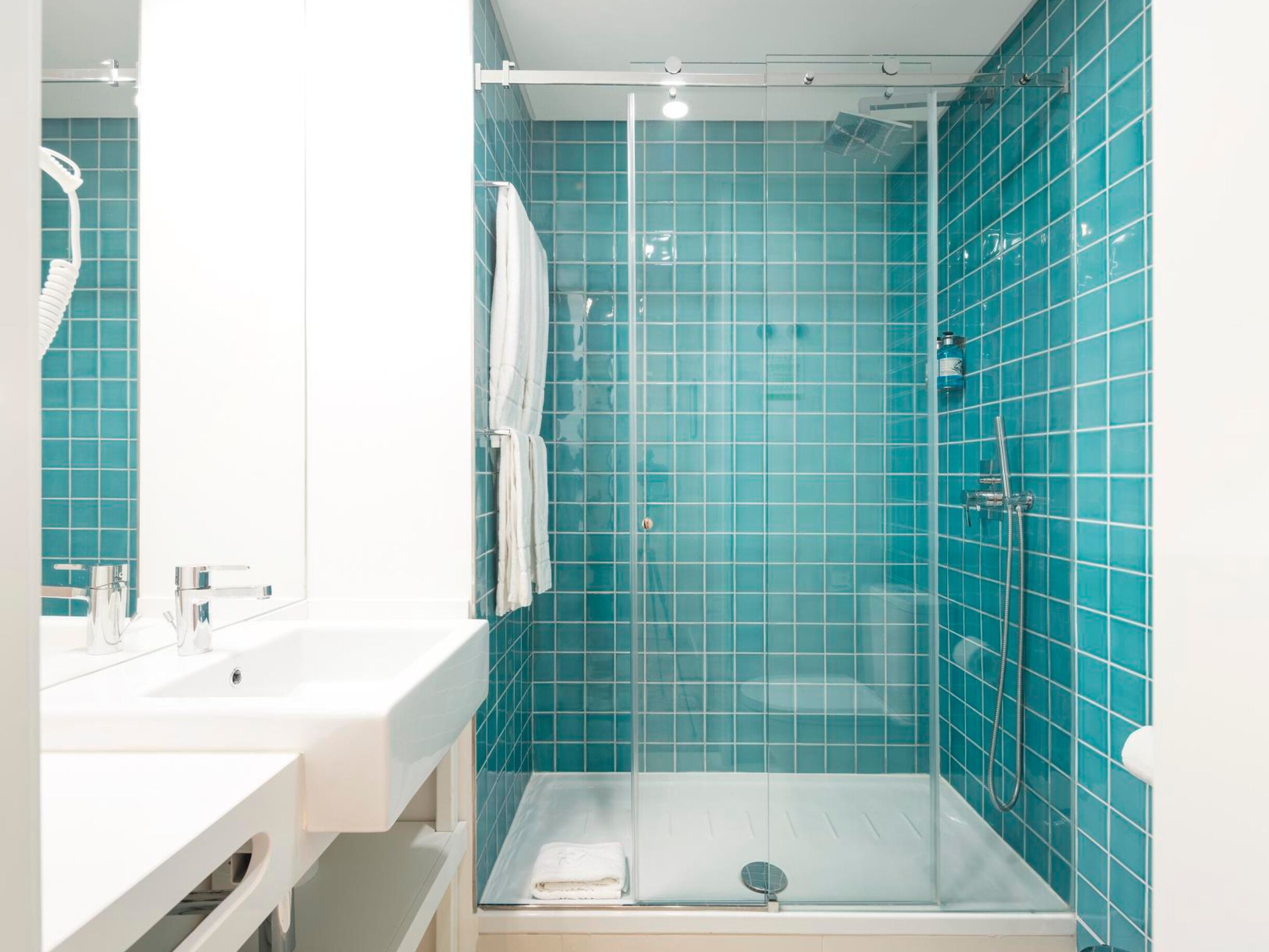 A bathroom with a glass-enclosed shower, white sink, and a mirror.