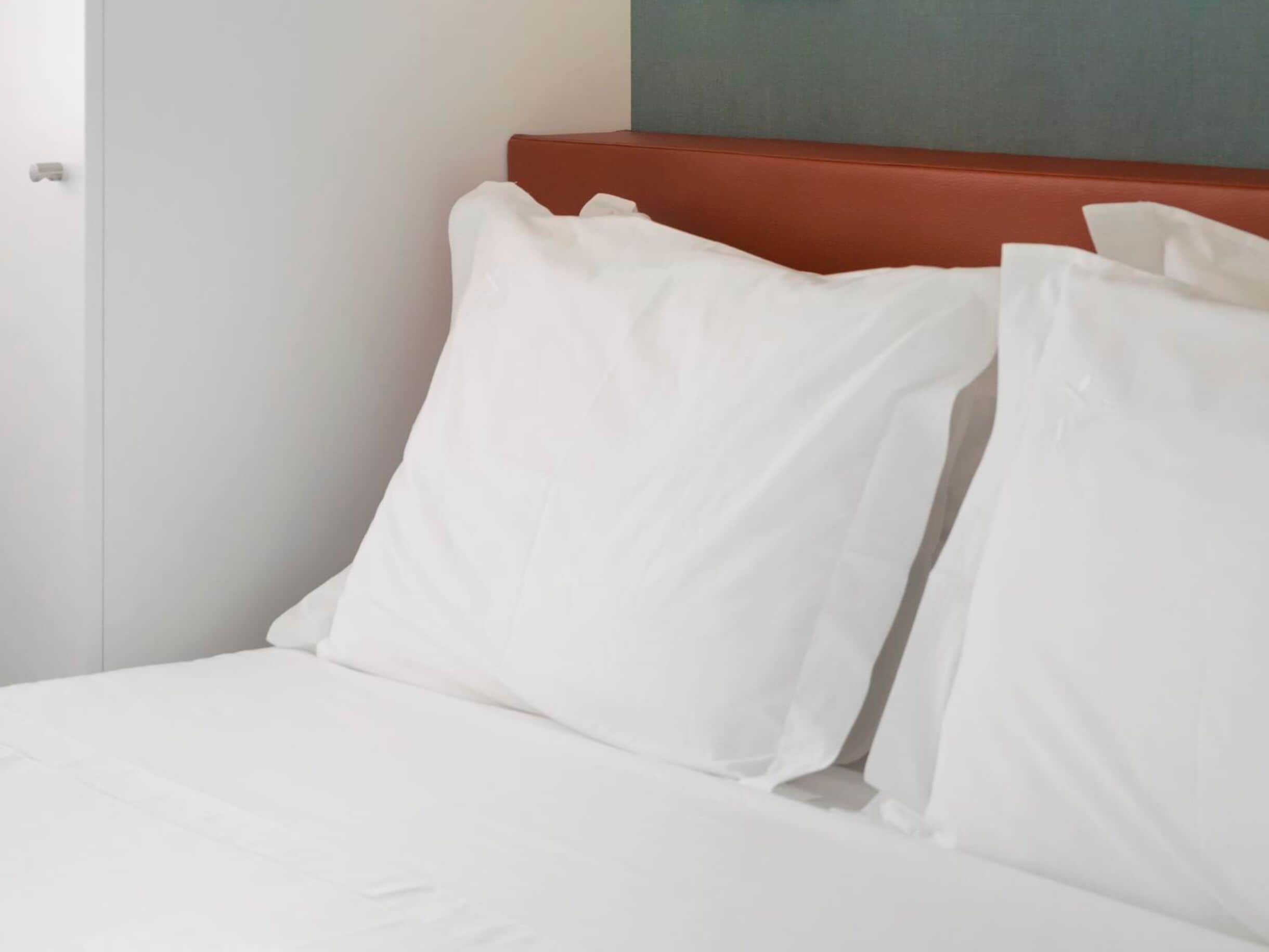 Una cama con ropa de cama y almohadas blancas, un cabecero rojo y una pared lisa.