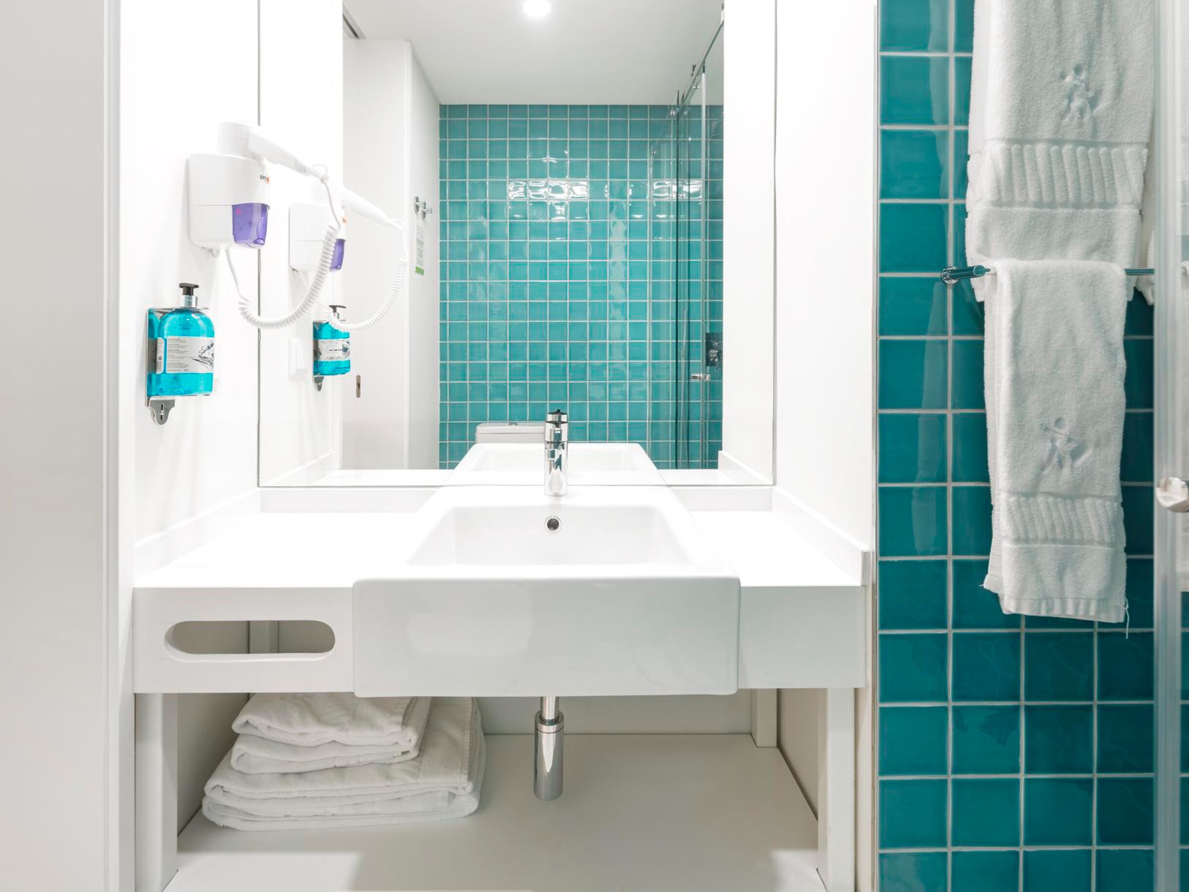 Een badkamer met een witte wasbak, een spiegel en een douchegedeelte met blauwe tegels.