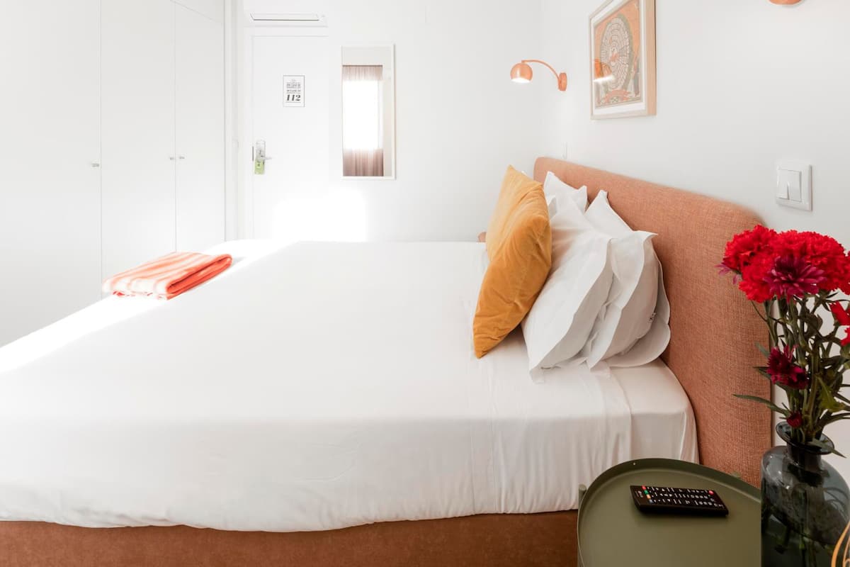 Habitación de hotel con una cama grande, una mesita de noche con control remoto, un jarrón con flores y un cuadro en la pared.