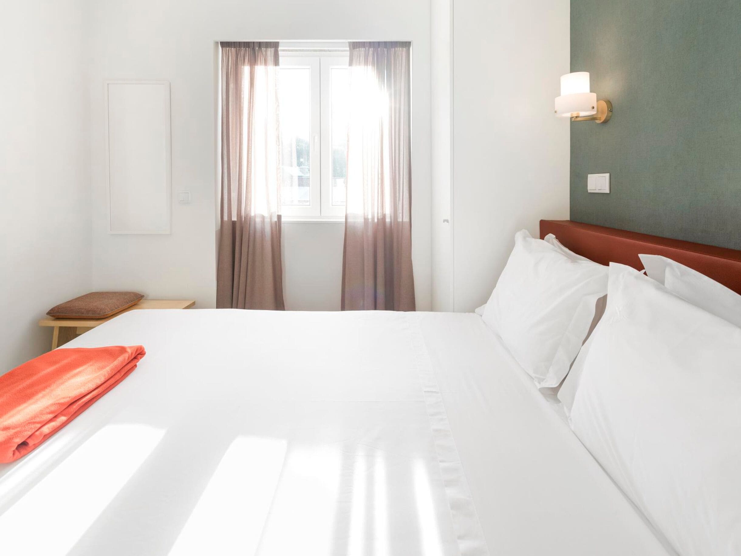 Une chambre d’hôtel avec un grand lit, une table de chevet, une serviette rouge et une fenêtre avec des rideaux.