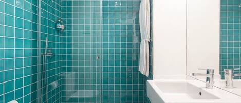 A bathroom with teal tiles, a glass shower enclosure, a white sink, and a mirror.