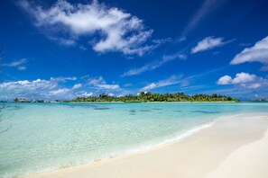 Una playa con agua turquesa cristalina, arena blanca y una pequeña isla con árboles al fondo.