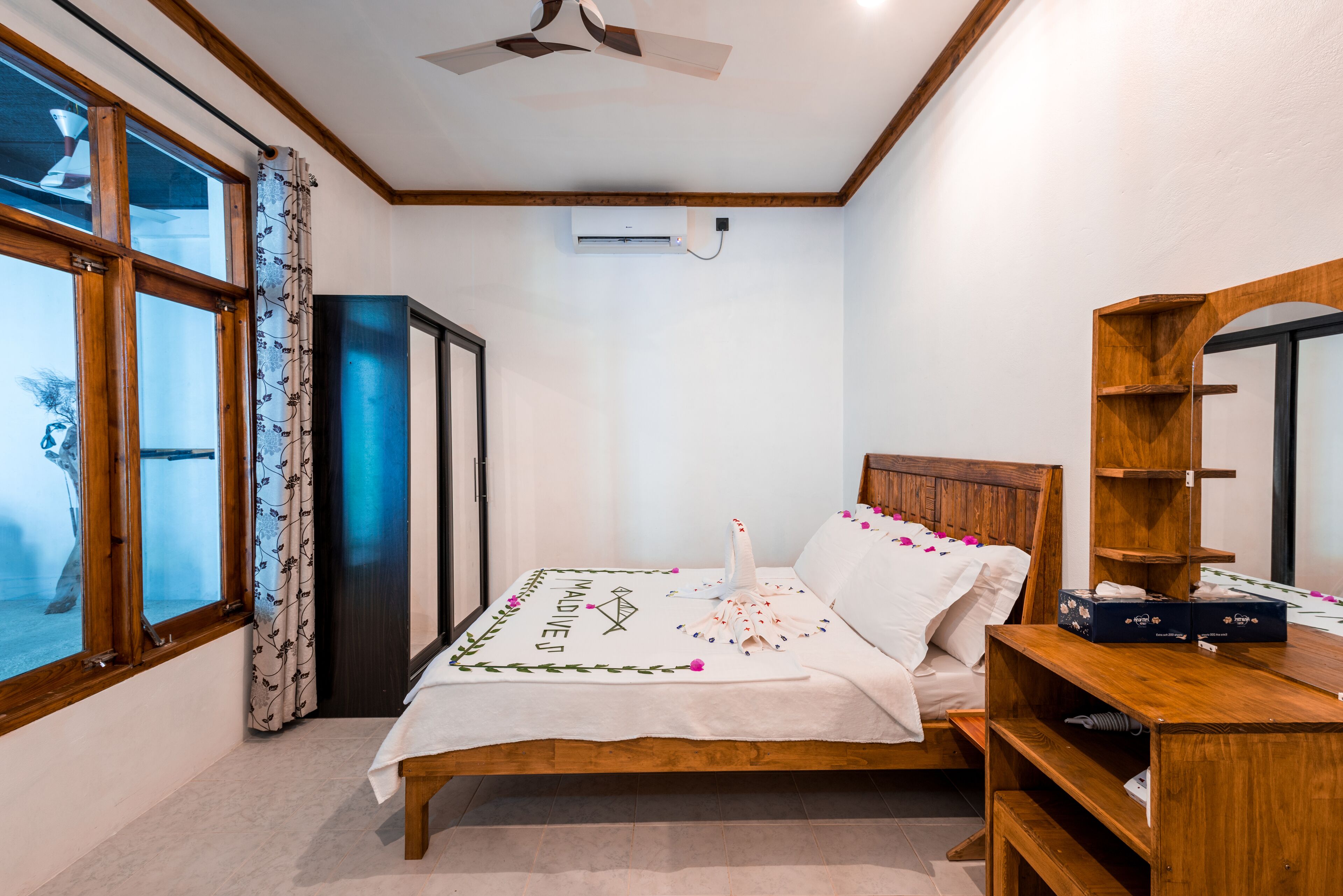 A bedroom with a bed, a wooden headboard, a wardrobe, a mirror, and a window with curtains.